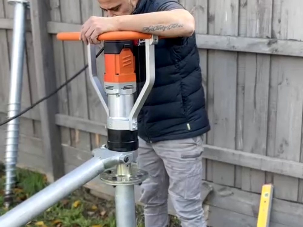 Pro Screw handheld driver being operated on a galvanised screw pile, with a driven pile alongside