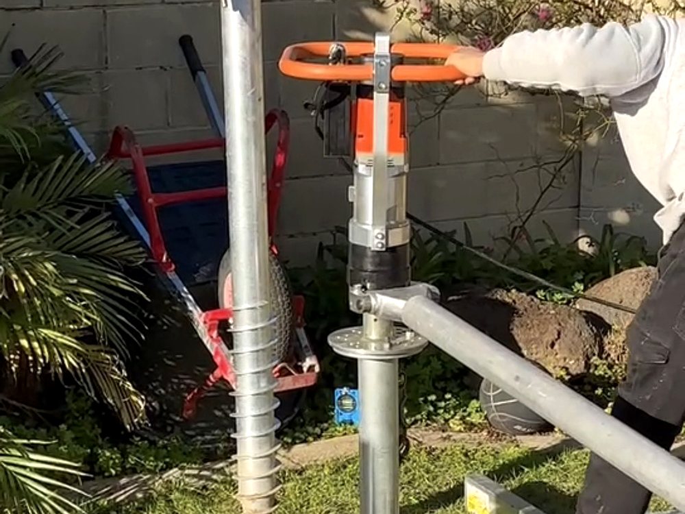 Full length galvanised screw pile standing beside the handheld driver mid install